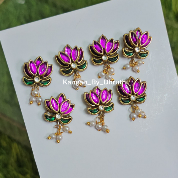 lotus flower hai pins with pink and green enamel details and small pearl-like drops, displayed on a white card held by a hand against a green grassy background.