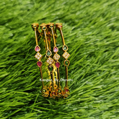 A set of gold-plated Indian bangles decorated with red, green, and clear stones, displayed on a green grass background. Ruby Pink & Emerald Green Micro-Gold Plated Temple Bangles