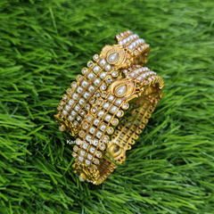 A stack of ornate gold-toned bangles decorated with white faux pearls and clear rhinestones, displayed on a textured green grass-like surface. White Pearl Micro-Gold Plated Peacock Bangles